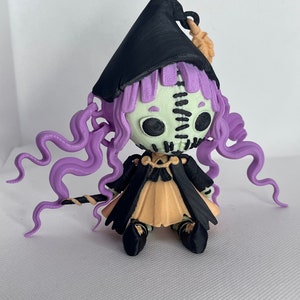 May include: A 3D printed figurine of a witch with purple hair, a black hat, and a black and orange dress. The witch is holding a stick in her hand.
