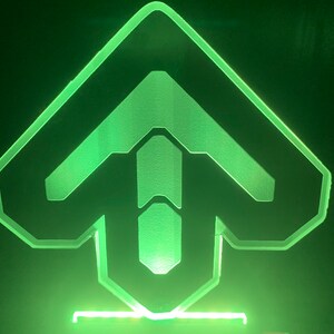 May include: A green illuminated acrylic sign with a stylized arrow pointing upwards. The sign is on a black background.