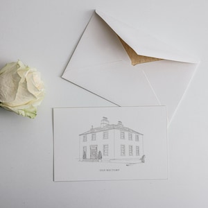 May include: A white rose and a greeting card with an envelope are arranged on a white surface. The card shows a detailed sketch of a building, labelled "OLD RECTORY." The envelope is white with a gold interior.