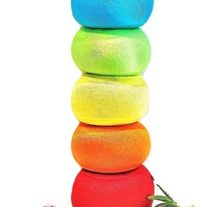 May include: A stack of seven colorful, round, fabric cushions in a rainbow pattern. The cushions are stacked from purple to red, with lavender sprigs in front.