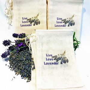 Peut inclure: Un lot de six sachets en lin naturel avec le texte "Live Love Lavender" et une branche de lavande violette imprimée sur chaque sachet. Des fleurs de lavande séchées sont éparpillées sur une surface blanche.