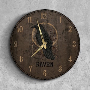 May include: A brown wooden clock with a black raven illustration and gold accents. The clock face has Roman numerals and the word "RAVEN" printed below the raven.