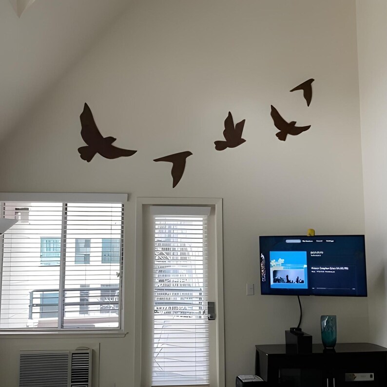 May include: A white wall with five brown bird silhouettes in flight. The birds are arranged in a diagonal line, with the largest bird at the top left and the smallest bird at the bottom right. A television screen is visible in the lower right corner of the image.