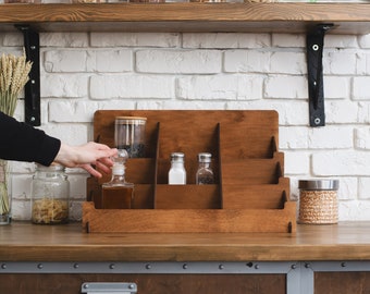 May include: A wooden countertop spice rack with five shelves. The rack is made of light brown wood and has a clear glass bottle with a cork stopper on the top shelf. There are two small salt and pepper shakers on the second shelf. The rack is sitting on a wooden countertop.