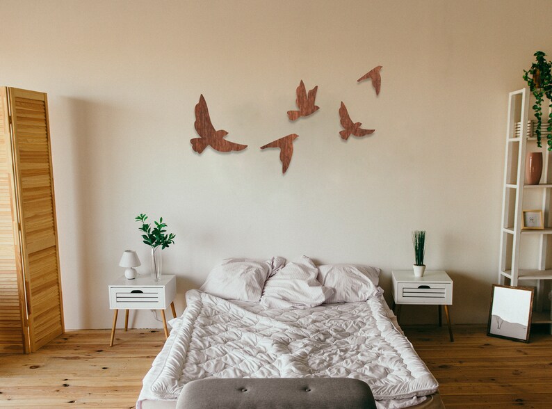 May include: A bedroom with a white bed and white nightstands. The wall above the bed is decorated with wooden bird cutouts in flight.