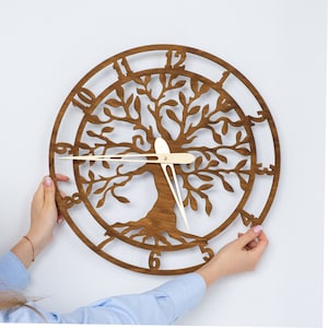 May include: A wooden wall clock with a tree of life design. The clock face features Roman numerals and a gold-colored hour and minute hand.