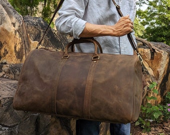 May include: A brown leather duffel bag with a long adjustable strap. The bag has a top handle and two side pockets. The bag is made of distressed leather and has a vintage look.