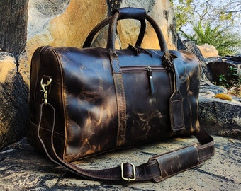 Può includere: Una borsa da viaggio in pelle marrone con manico superiore e tracolla. La borsa ha un aspetto invecchiato ed è realizzata in pelle di alta qualità.