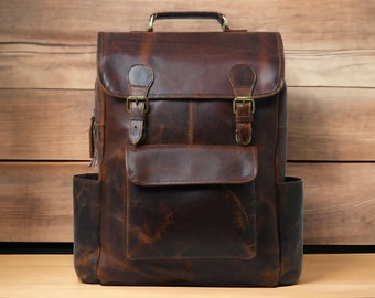 Könnte beinhalten: Ein brauner Lederrucksack mit zwei großen Fronttaschen und zwei verstellbaren Schnallen auf der vorderen Klappe. Der Rucksack hat einen Used-Look und ist aus hochwertigem Leder gefertigt.