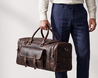 Pode incluir: Uma mala de viagem de couro castanho escuro com duas alças superiores, um bolso frontal grande com duas tiras de fivela e fechos laterais. A mala tem uma forma retangular com costuras reforçadas e detalhes em metal nas tiras e nos fechos.