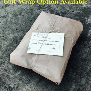 K&ouml;nnte beinhalten: Ein Geschenk, verpackt in braunem Papier, mit Bindfaden verschn&uuml;rt und einer kleinen Karte. Die Karte lautet "Gift Message: Here's to a year of blessings and beyond. Have a Merry Christmas! -Sam". Der Text "Gift Wrap Option Available" ist gelb.