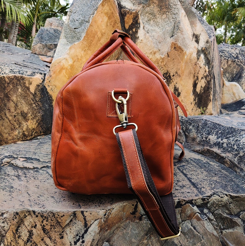 May include: A brown leather duffel bag with a long adjustable strap. The bag has a brass buckle and a top handle.