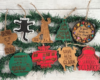 May include: A set of nine wooden Christmas ornaments featuring characters and quotes from the movie 'Christmas Vacation'. The ornaments are painted in various colors, including red, green, and brown. The ornaments feature phrases like 'Save the Neck for Me Clark', 'You Serious Clark?', and 'Is your house on fire, Clark?'