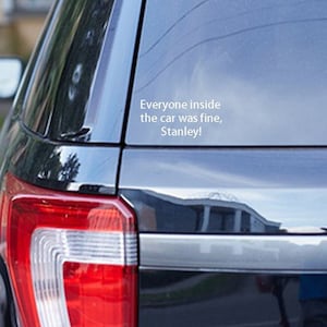 May include: A black SUV with a white vinyl sticker on the back window that reads "Everyone inside the car was fine. Stanley!"
