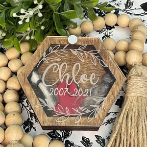 May include: A hexagonal wooden box with a glass top, featuring a red heart and a white inscription that reads "Chloe 2007-2021". The box is decorated with a white floral design and has a silver latch.