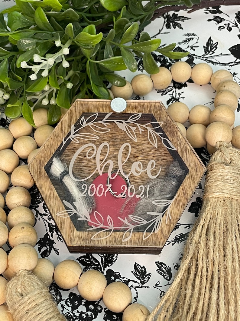 May include: A hexagonal wooden box with a glass top, featuring a red heart and a white inscription that reads "Chloe 2007-2021". The box is decorated with a white floral design and has a silver latch.