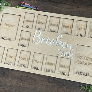 Puede incluir: Un marco de fotos de madera con ranuras para fotos de cada grado escolar, desde preescolar hasta la graduaci&oacute;n de la escuela secundaria. El marco est&aacute; personalizado con los nombres "Brecken Zane".