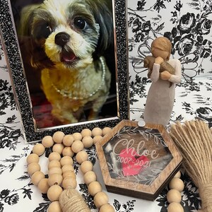 May include: A wooden hexagonal box with a clear lid and a red heart inside. The box has the name "Chloe" engraved on it, along with the dates "2007-2021". The box is surrounded by a wooden bead garland with tassels.