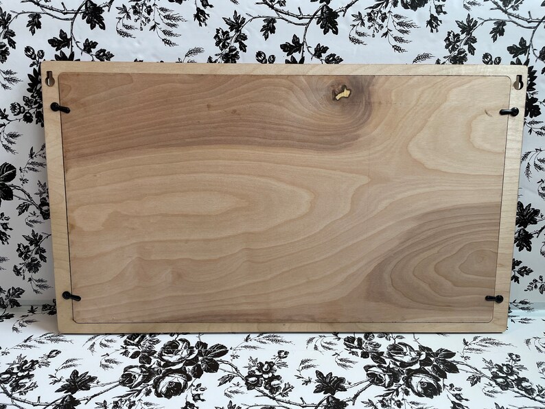 Puede incluir: Un letrero de madera de color marr&oacute;n claro con un borde marr&oacute;n oscuro. El letrero tiene cuatro peque&ntilde;os ganchos de metal negro en las esquinas.