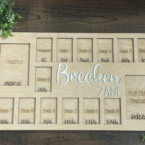 Puede incluir: Un marco de fotos de madera con ranuras para fotos de cada grado escolar, desde preescolar hasta la graduaci&oacute;n de la escuela secundaria. El marco est&aacute; personalizado con los nombres "Brecken Zane".