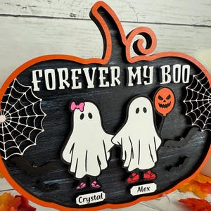 May include: A Halloween-themed wooden sign in the shape of a pumpkin. The sign features the phrase "FOREVER MY BOO" and two ghost figures holding hands. One ghost has a pink bow and the other holds a jack-o'-lantern balloon. The sign is decorated with spiderwebs and bats.