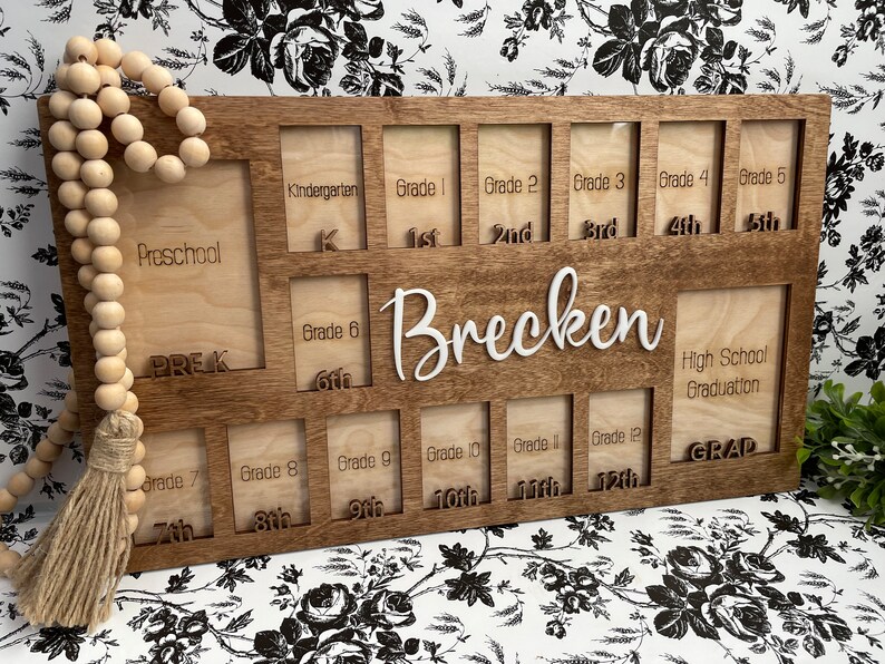 Puede incluir: Un marco de fotos de madera con 14 ranuras para fotos, etiquetadas con los grados desde preescolar hasta la graduaci&oacute;n de la escuela secundaria. El marco est&aacute; personalizado con el nombre "Brecken".