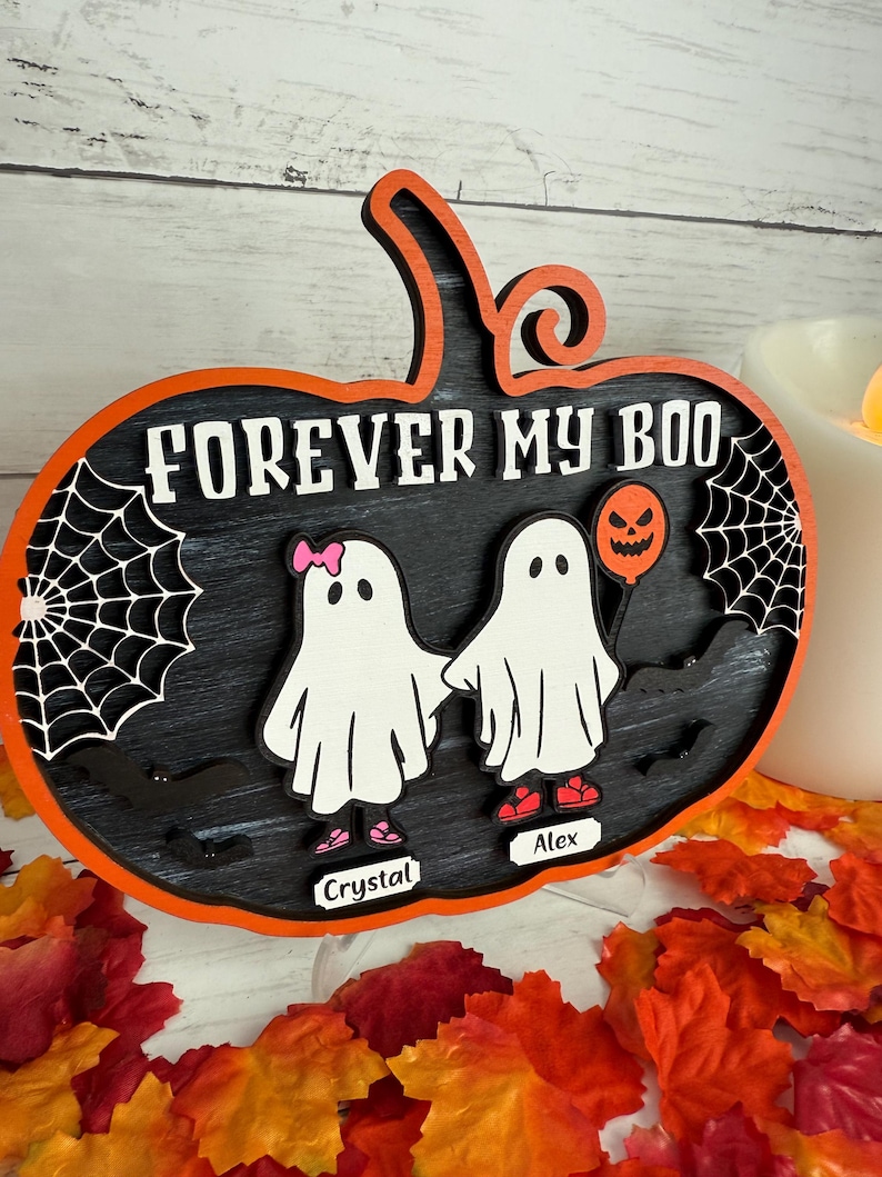 May include: A Halloween-themed wooden sign in the shape of a pumpkin. The sign is black with orange trim and features the text "FOREVER MY BOO" in white. Two ghost figures are holding hands. One ghost has a pink bow and the other holds a pumpkin balloon.