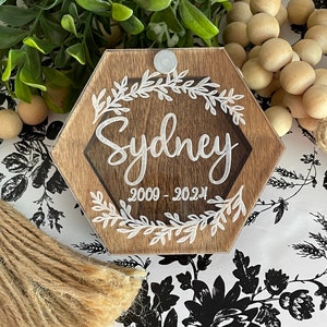 May include: A hexagonal wooden plaque with a clear acrylic insert. The plaque has a white floral design and the text "Sydney 2009 - 2024" in white lettering.