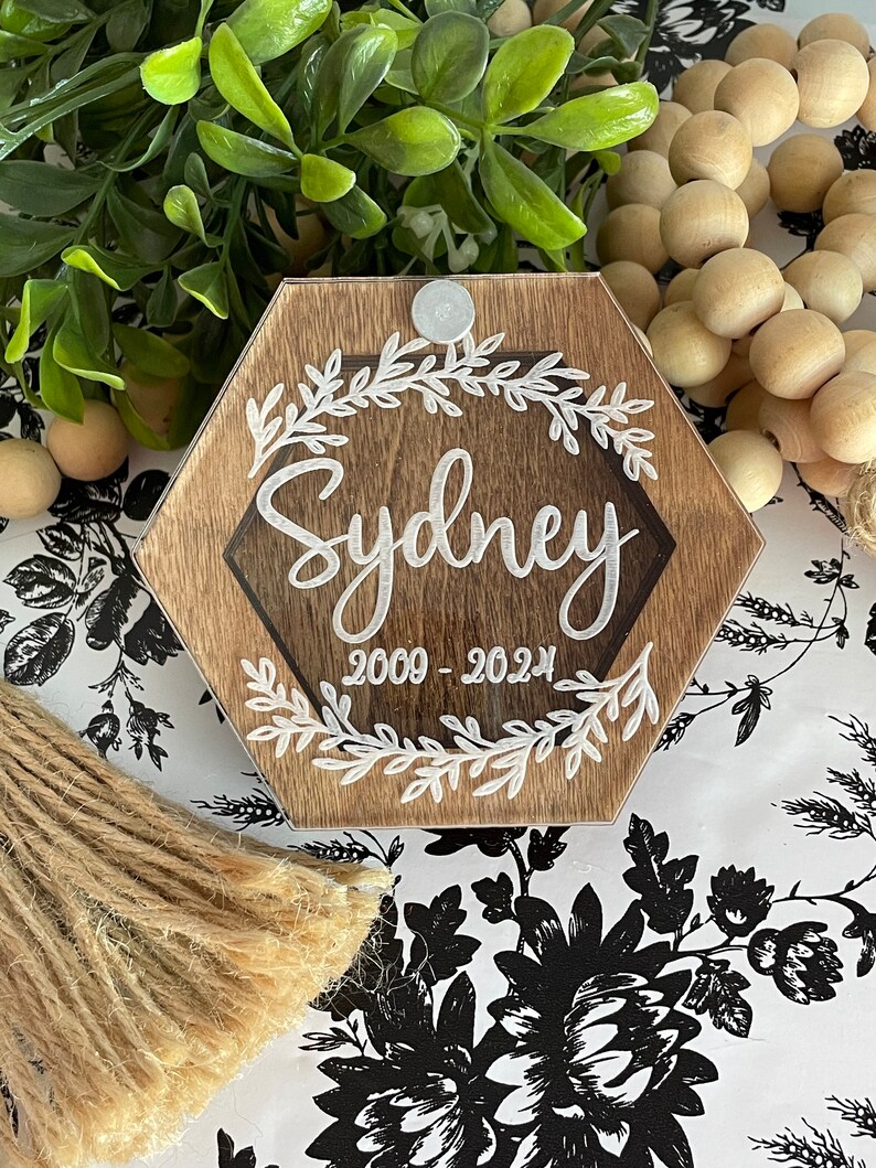 May include: A hexagonal wooden plaque with a clear acrylic insert. The plaque has a white floral design and the text "Sydney 2009 - 2024" in white lettering.