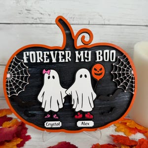 May include: A Halloween-themed pumpkin-shaped wooden sign with the text "FOREVER MY BOO". It features two ghost figures holding hands, a spider web, and a jack-o'-lantern balloon. The names "Crystal" and "Alex" are below the ghosts.