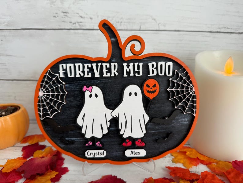 May include: A Halloween-themed pumpkin-shaped wooden sign with the text "FOREVER MY BOO". It features two ghost figures holding hands, a spider web, and a jack-o'-lantern balloon. The names "Crystal" and "Alex" are below the ghosts.