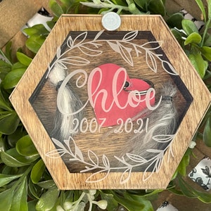 May include: A wooden hexagonal box with a glass insert. The box has a white inscription that reads "Chloe 2007-2021" and a red heart inside. The box is surrounded by a leafy design.