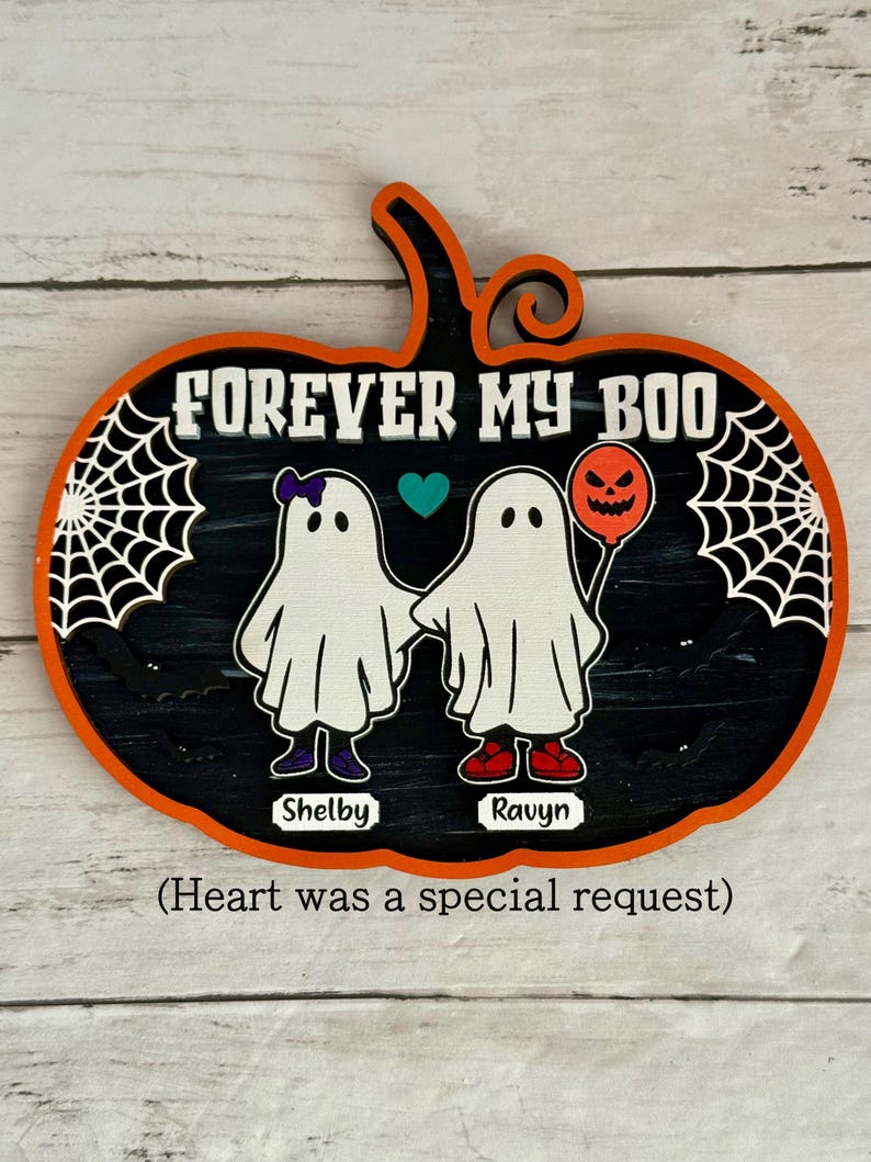 May include: A Halloween-themed pumpkin-shaped wooden sign with the text "FOREVER MY BOO". It features two ghost figures holding hands, with the names "Shelby" and "Ravyn" below. One ghost has a purple bow and the other holds a jack-o'-lantern balloon.
