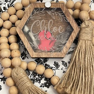 May include: A hexagonal wooden box with a clear lid and a red heart inside. The box is decorated with a floral design and the name "Chloe" and the dates "2007 2021".