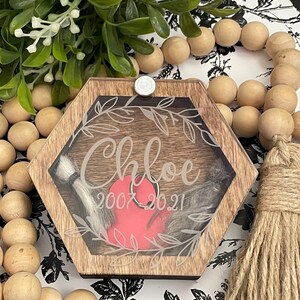 May include: A hexagonal wooden box with a clear lid, featuring a heart-shaped compartment and the inscription "Chloe 2007 2021".