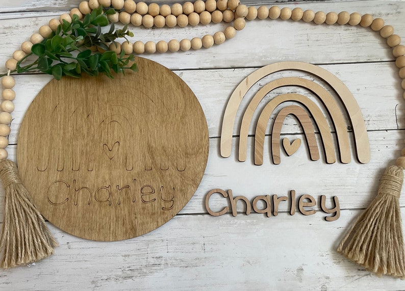 May include: Wooden rainbow wall decor with a heart in the center and the name Charley written in cursive on a separate piece of wood. The name Charley is also written on a round wooden plaque with a rainbow design.
