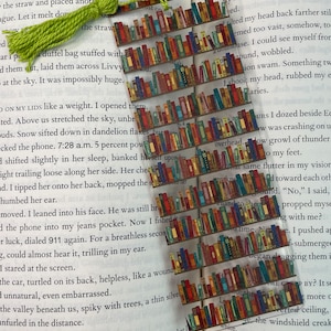 May include: A green tassel bookmark with a colorful image of a bookshelf filled with books. The bookmark is placed on a page of a book with text about a car accident.