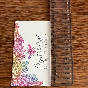 K&ouml;nnte beinhalten: Eine wei&szlig;e Visitenkarte mit einem regenbogenfarbenen Glitzer-Wabenmuster, einer Bienenillustration und dem Text "Crystal Pugh Design Cut Craft".
