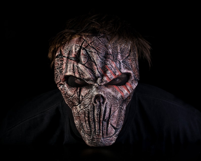 May include: A person wearing a scary, detailed, gray and red skull mask with a black background.