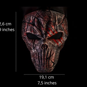 May include: A red and black skull mask with a textured surface and red paint streaks. The mask is 8.9 inches tall and 7.5 inches wide.
