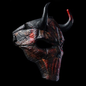 K&ouml;nnte beinhalten: Eine schwarze und rote Teufelmaske mit H&ouml;rnern. Die Maske ist aus einem strukturierten Material gefertigt und hat ein detailliertes Design.