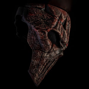 May include: A red and black Halloween mask with a textured, skeletal design. The mask has a strap for wearing.