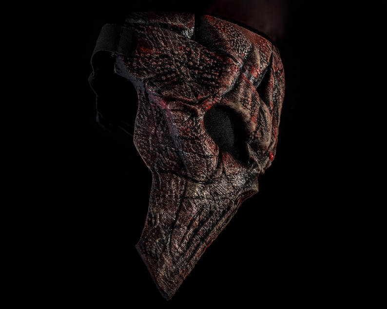 May include: A red and black Halloween mask with a textured, skeletal design. The mask has a strap for wearing.