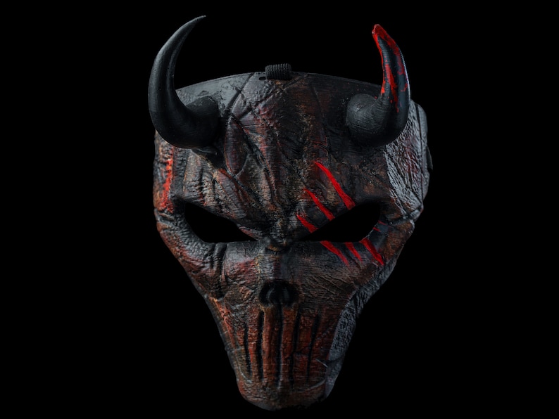 K&ouml;nnte beinhalten: Eine schwarze und rote Teufelmaske mit H&ouml;rnern. Die Maske hat eine strukturierte Oberfl&auml;che und rote Farbakzente.