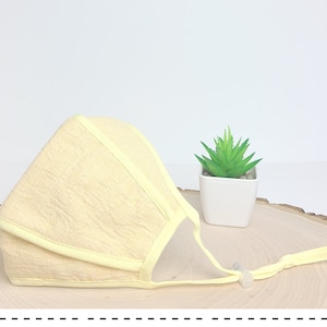 May include: A pale yellow face mask with a light yellow trim and adjustable straps. The mask is made of a soft, textured fabric.