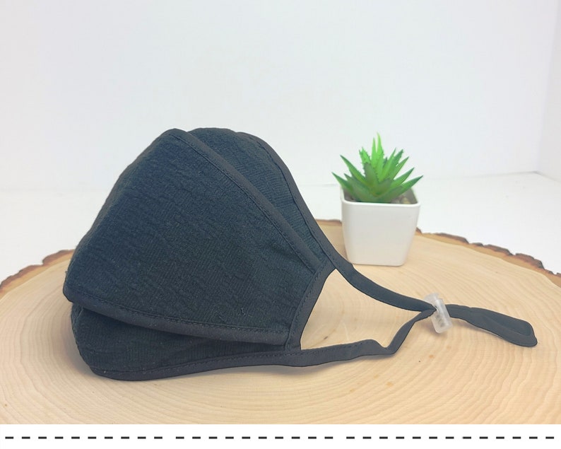 May include: Black face mask with a textured fabric and adjustable ear loops. The mask has a clear plastic nose wire and a black elastic strap.