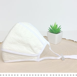 May include: White face mask with a textured fabric and white elastic straps. The mask has a white trim around the edges.