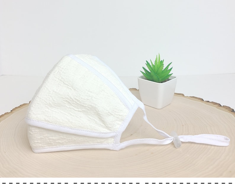May include: White face mask with a textured fabric and white elastic straps. The mask has a white trim around the edges.