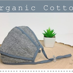 May include: A gray organic cotton face mask with adjustable ear loops and a nose wire. The mask is on a wooden surface with a small potted plant in the background. The text "Shop for Natures" is visible in the bottom right corner.