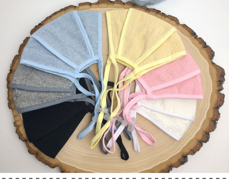 May include: A set of eight face masks in various colors, including light blue, yellow, pink, white, and gray. The masks are made of a soft, breathable fabric and have adjustable ear loops.